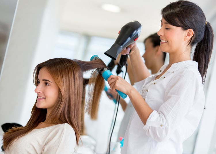Stylist drying hair of a female client at the beauty salon